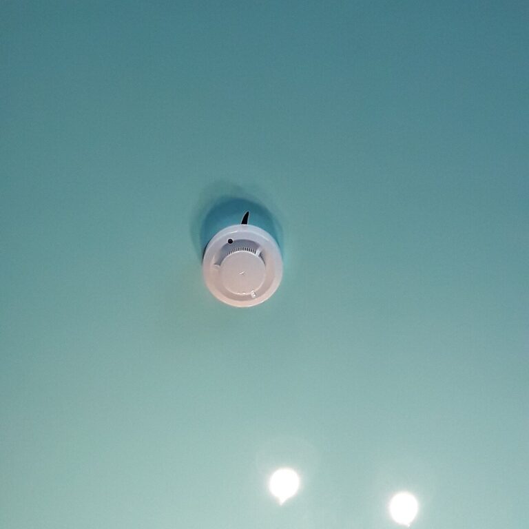 White round smoke detector mounted on a flat teal ceiling