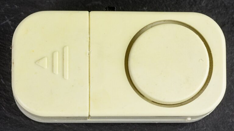 Top view of a cream-colored stand-alone magnetic contact alarm with a round buzzer, on a dark surface